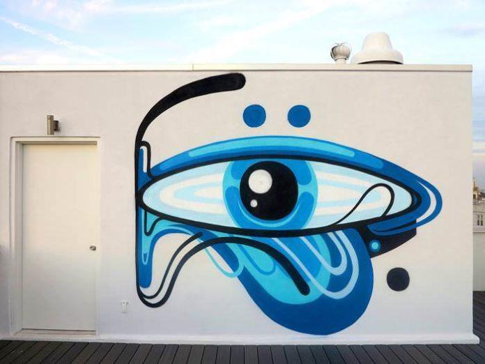 An eye in blue hues stares out from the side of this building in this graffiti mural by Reka One