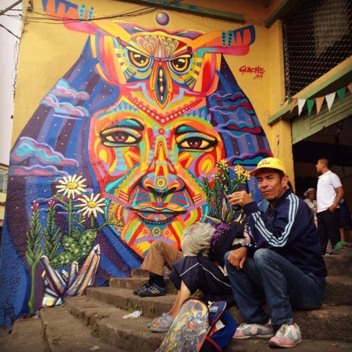 Street artist Guache paints a colorful graffiti mural of a tribal leader with an owl totem