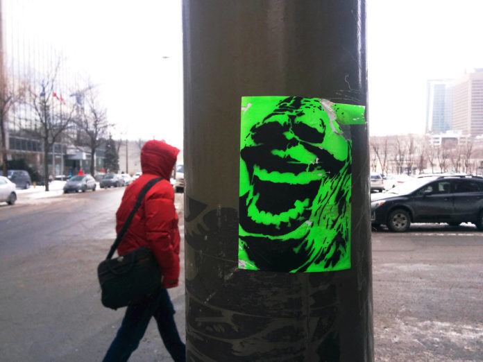 This stencilled Slimer sticker is a colorful street art work in the gray winter of Montréal