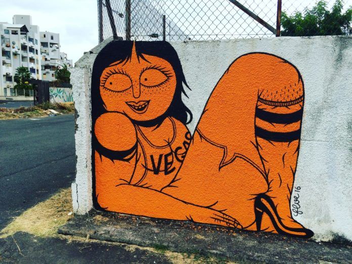 A busty cartoon lady poses in the corner of this wall in bright orange and black paint in typical Floe style
