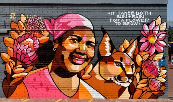 Surrounded by local South African proteas and a caracal cat, the motherly African woman in this street art mural by Nardstar seems happy and loving